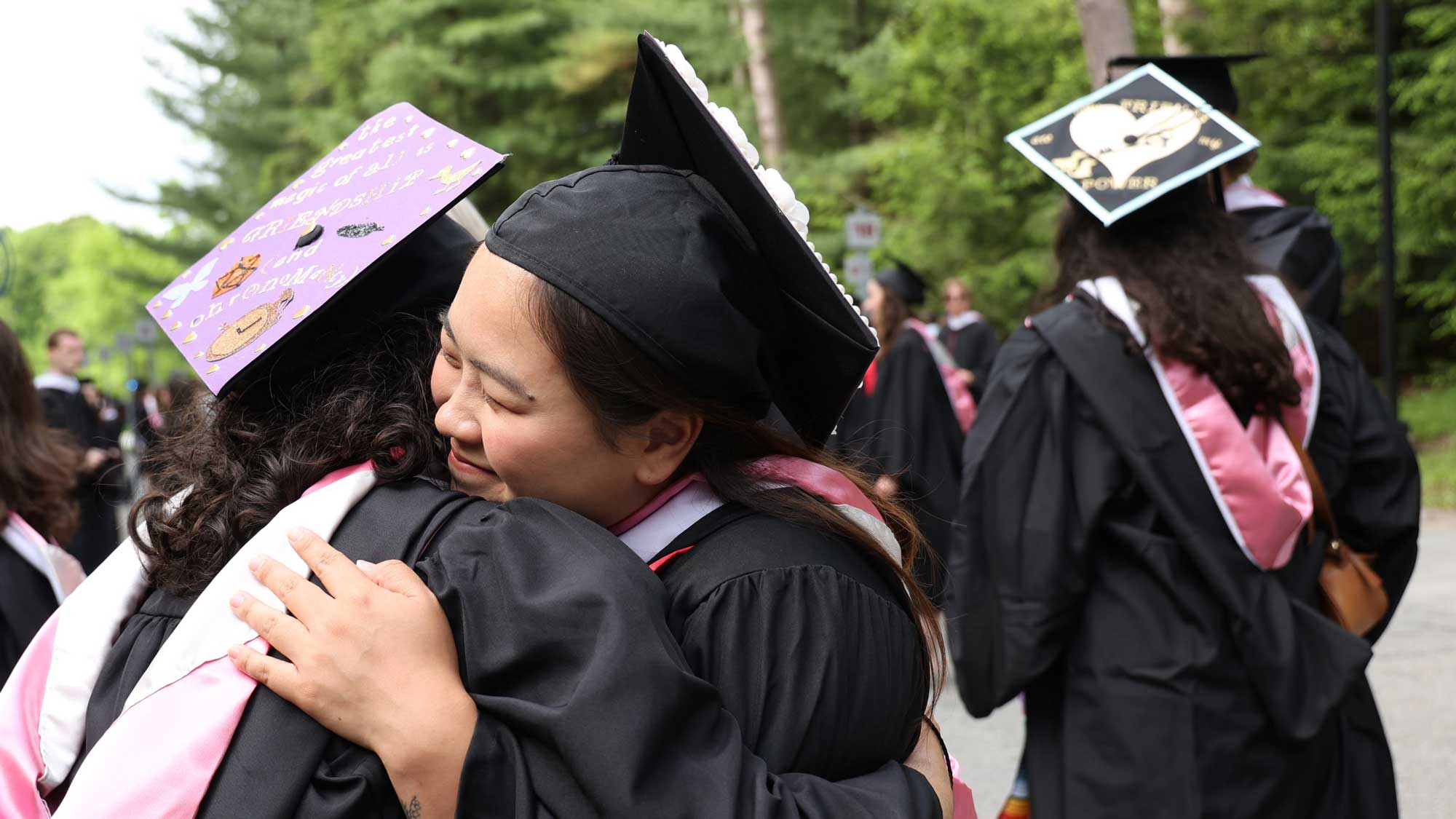 Two people in graduation ceremony attire embracing.