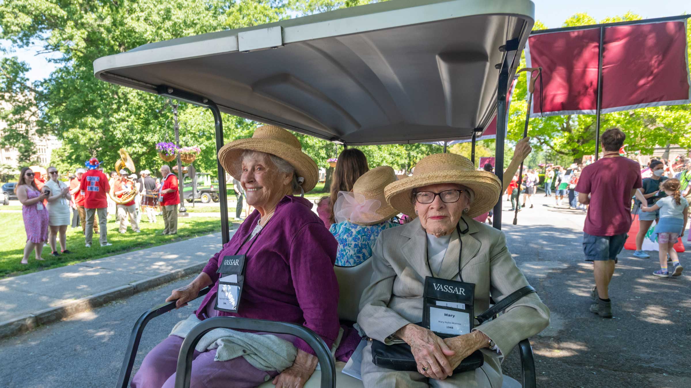 Two people wearing straw hats sitting in a golf cart looking on.