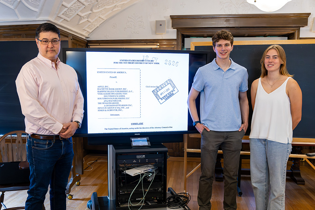 Professor and two students standing on either side of a presentation slide showing a legal document.