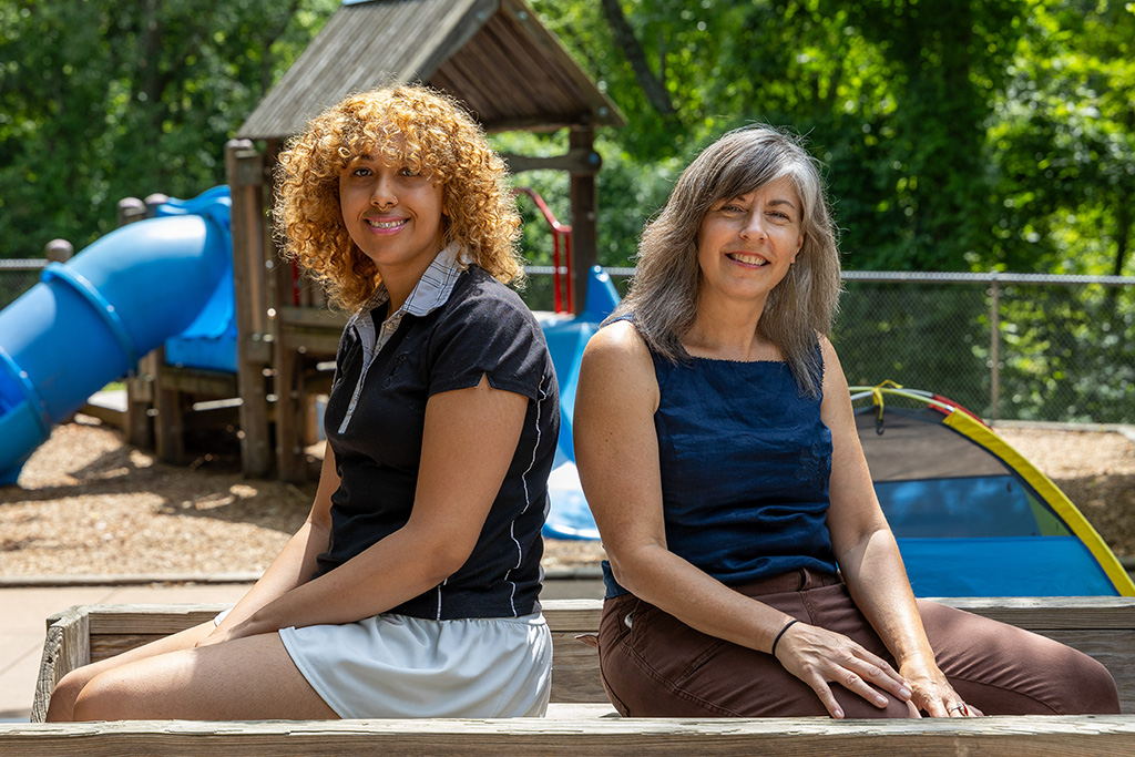 Student and professor seated facing the camera with a playground in the background.