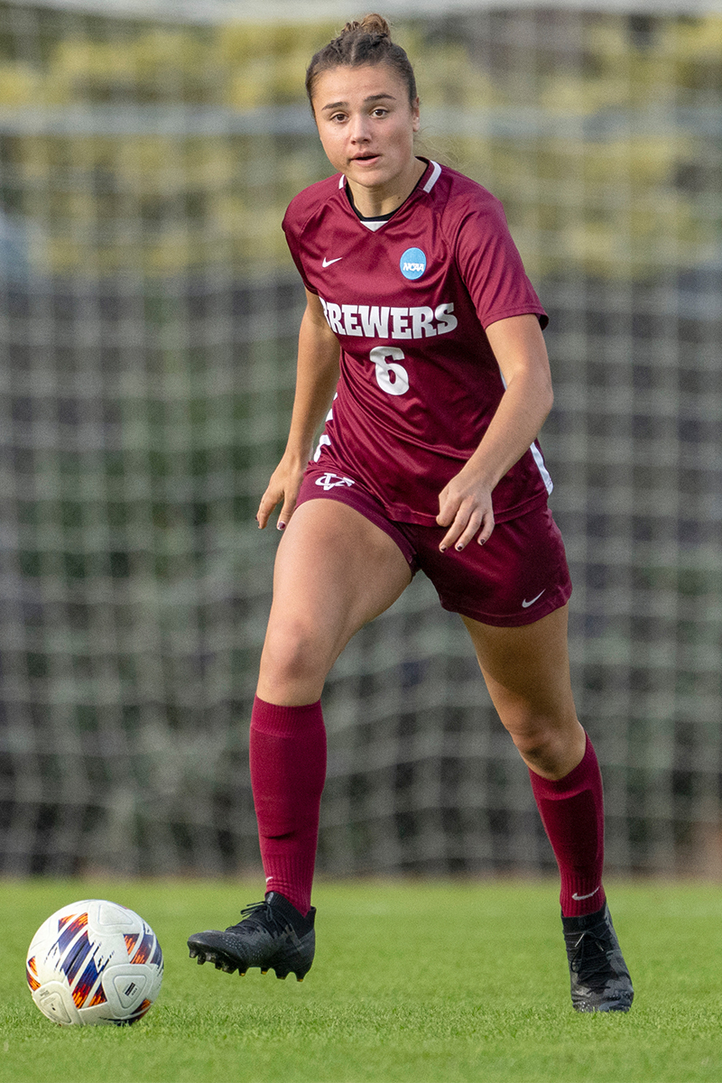A soccer player dribbles the ball on a grassy field during a game.
