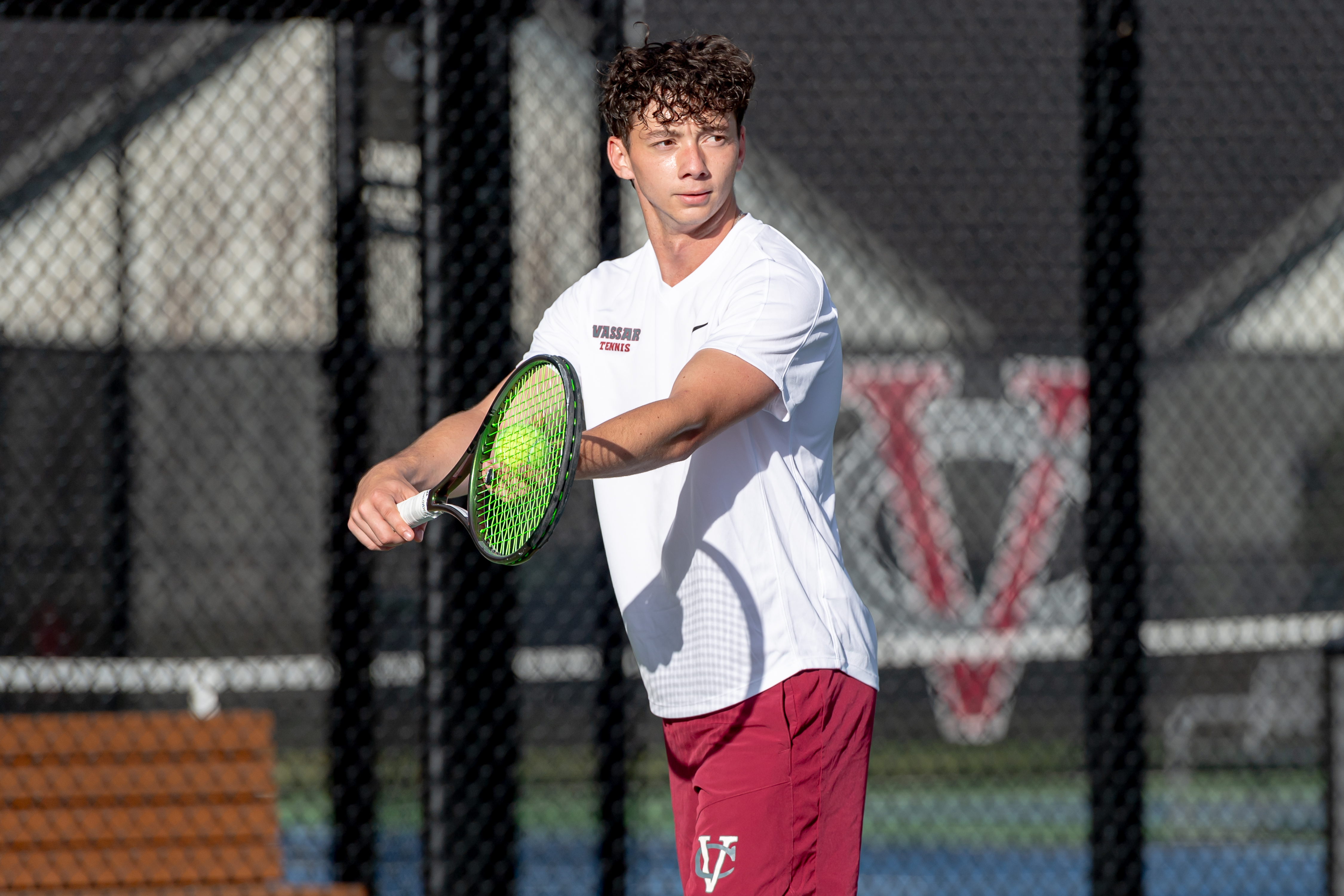 A tennis player holds a ball against his racket, getting ready to serve.