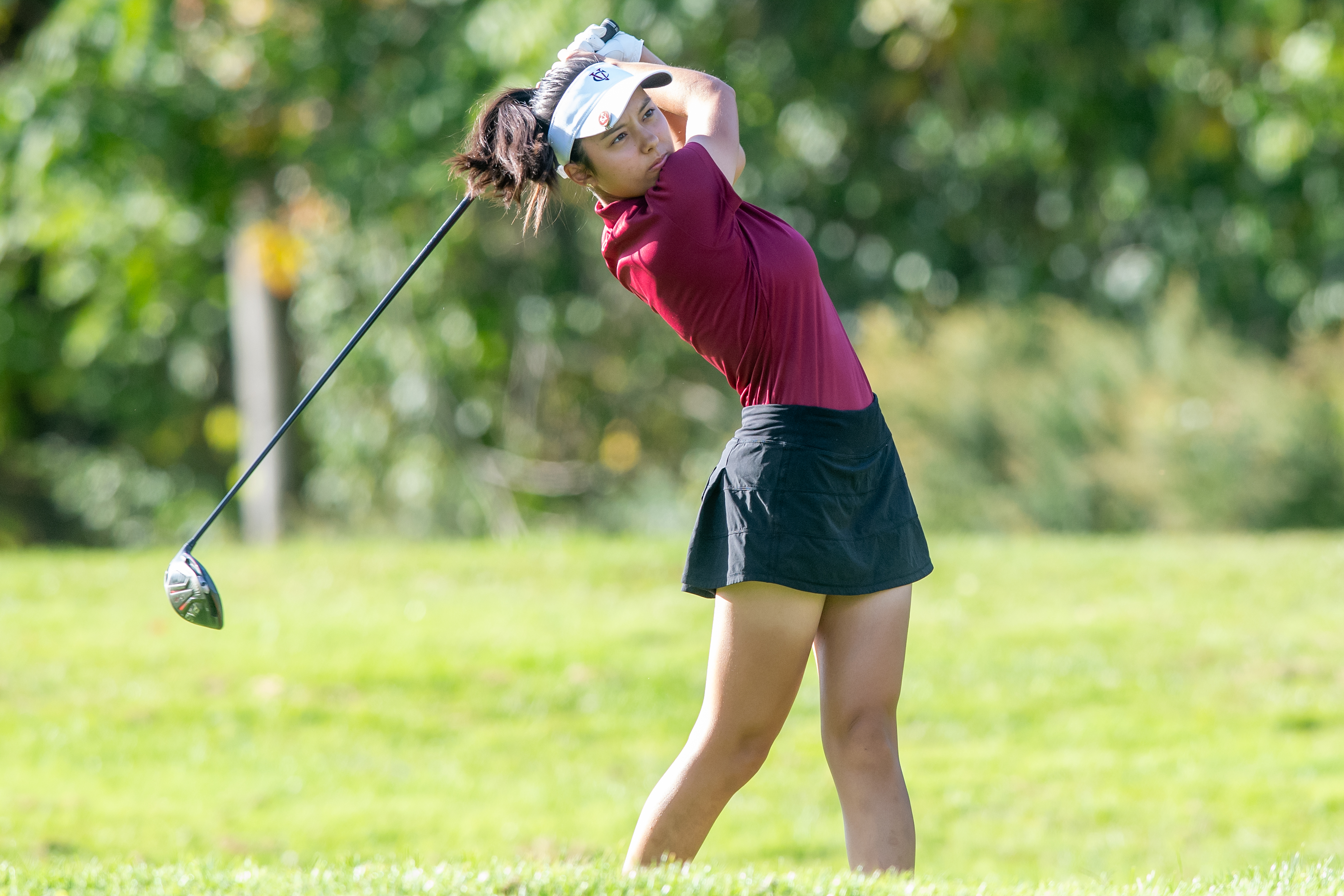 A golfer wearing a visor with club raised stares into the distance after hitting the ball.