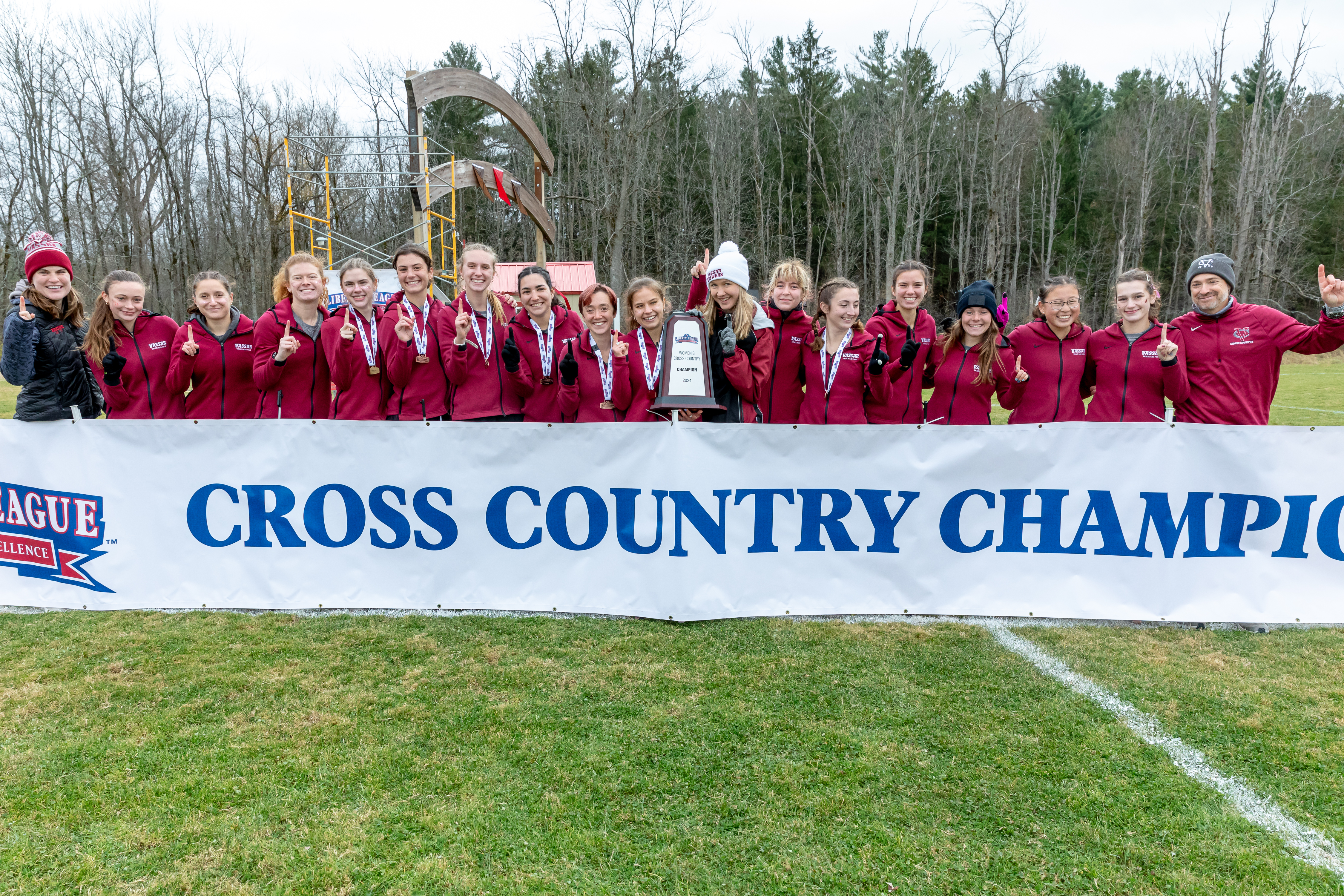 A group of Vassar athletes, some wearing medals, pose behind a banner that reads "Cross Country Champions."
