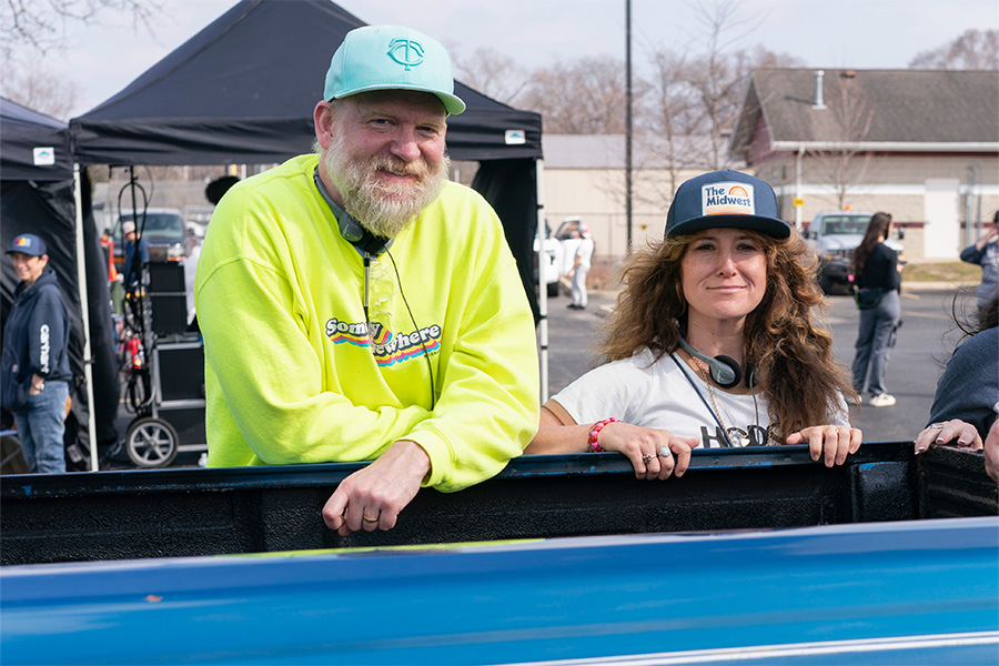 Paul Thureen '00 and Hannah Bos '00 on the set of their HBO show, Somebody Somewhere, both wearing baseball caps and smiling at the camera.