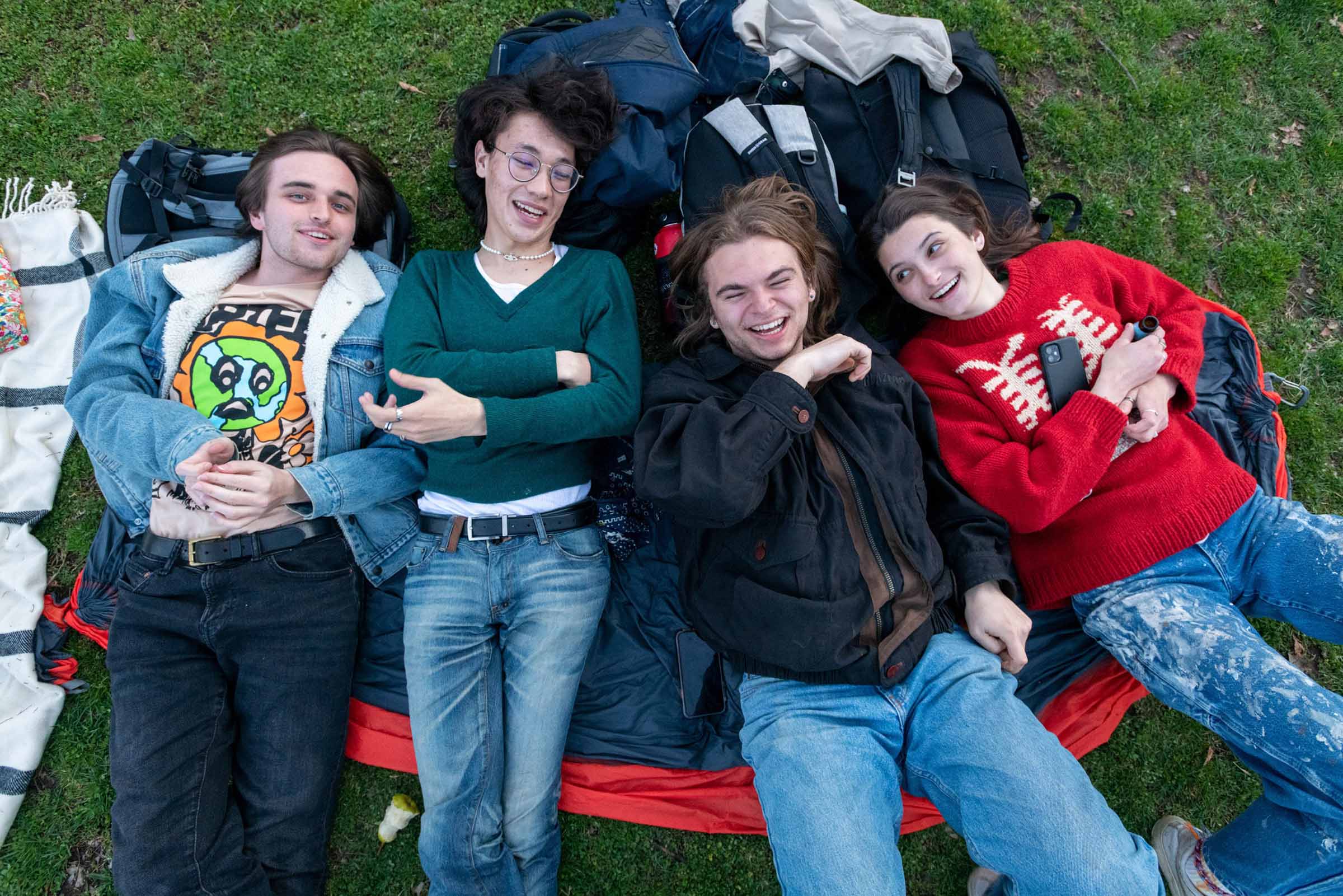 Four students lie on a blanket spread on the grass.