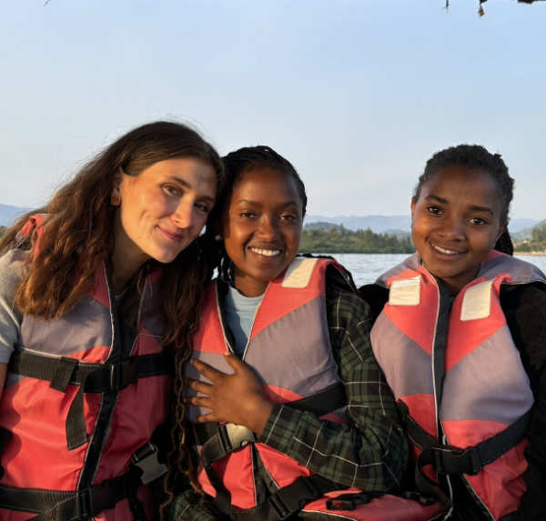Three people with life vests sit together in a boat on a river.