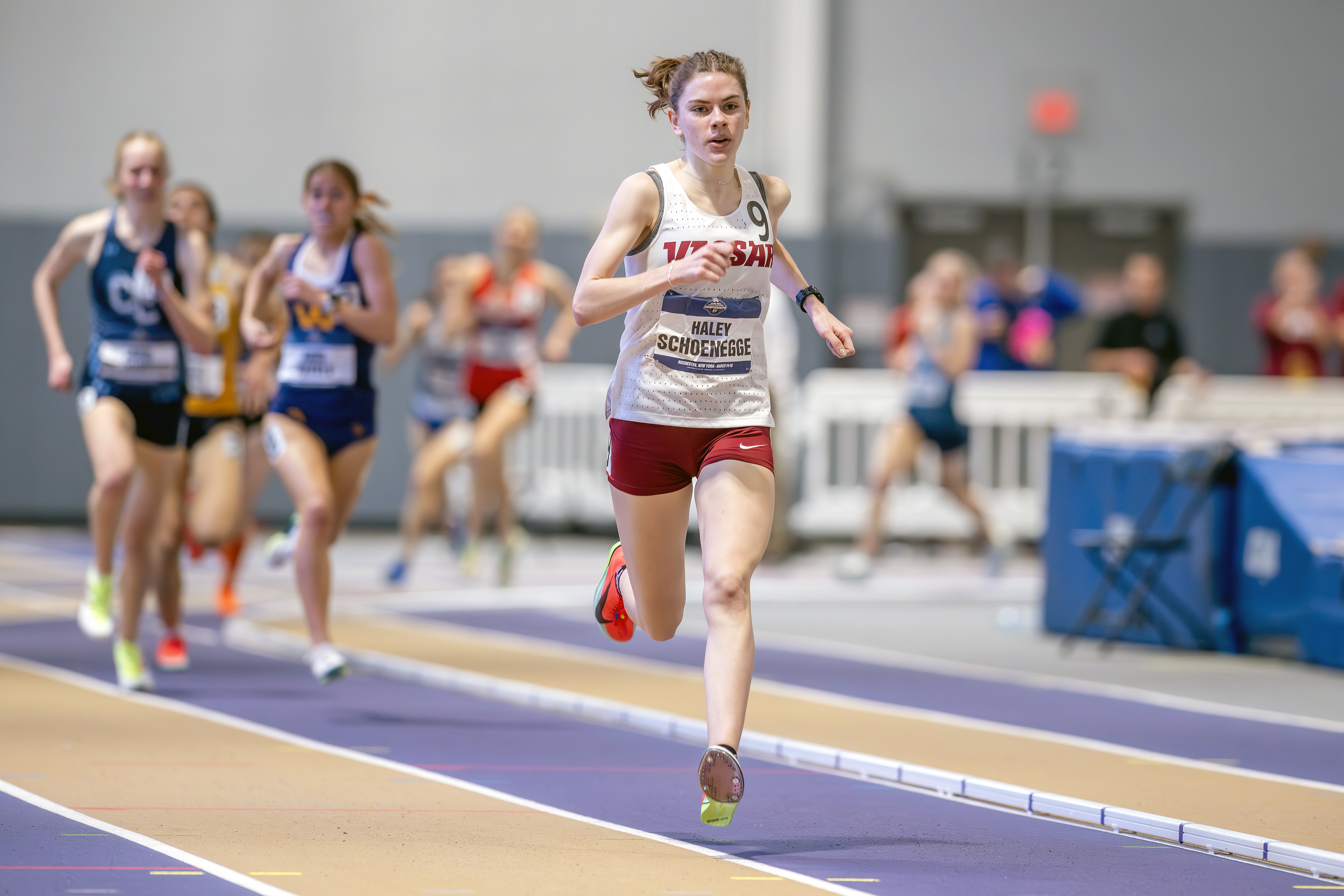 A woman running on an indoor track far ahead of her competitors.