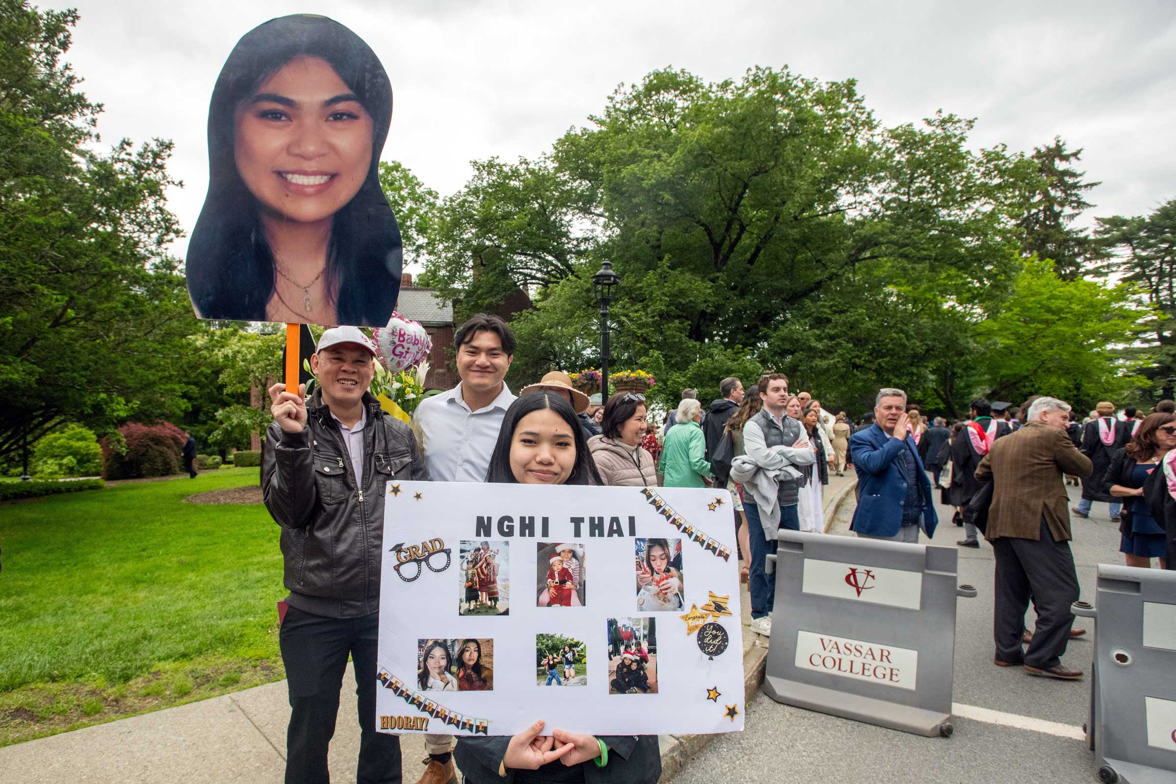 Person standing and holding a poster with photos and a sign with a large photo of a face attached to it.