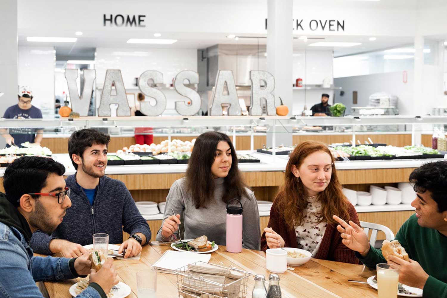 Group of people eating and visiting at a table in a cafeteria.