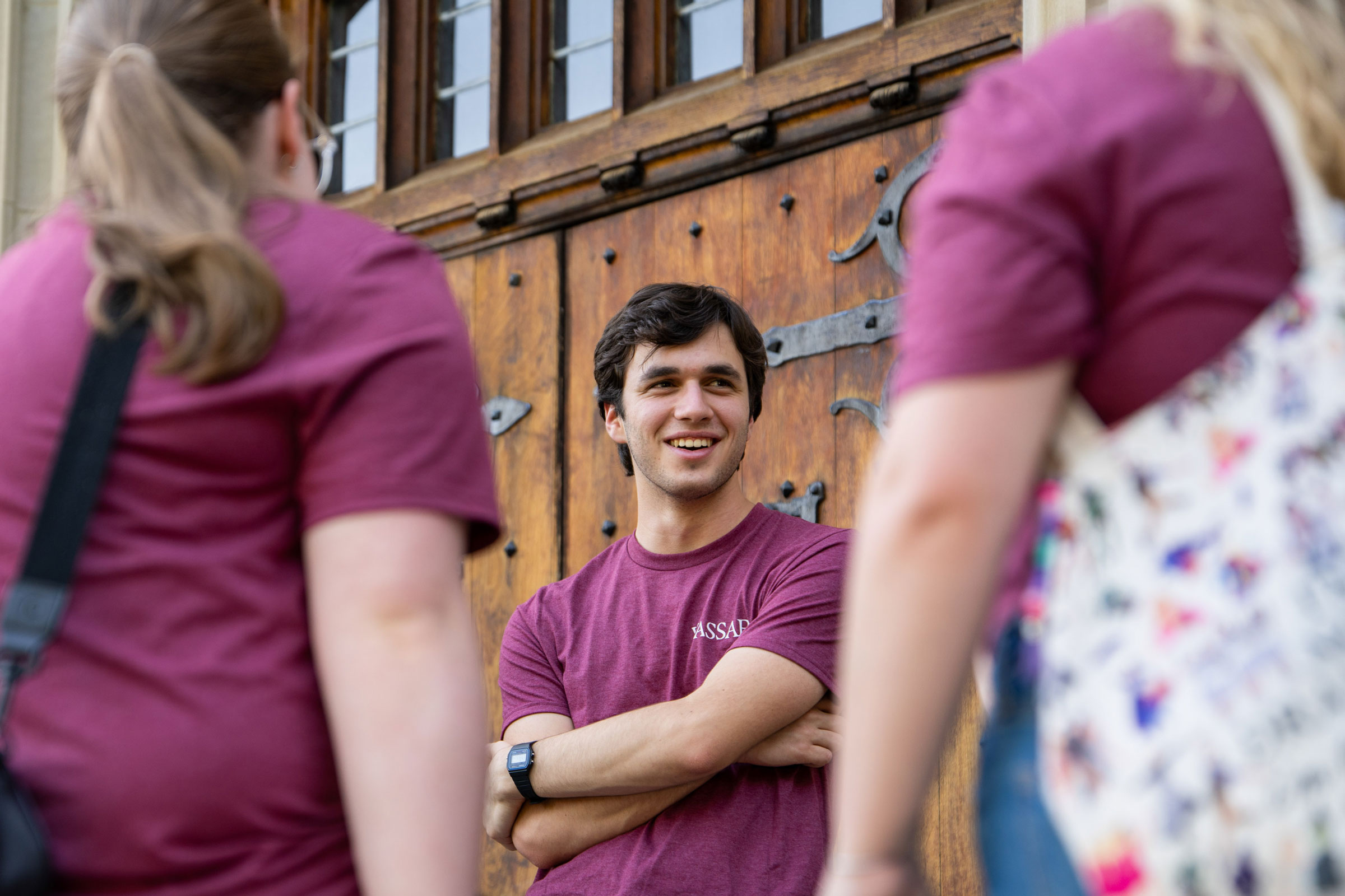 A smiling person standing with arms crossed talking to two people with their backs to the camera.