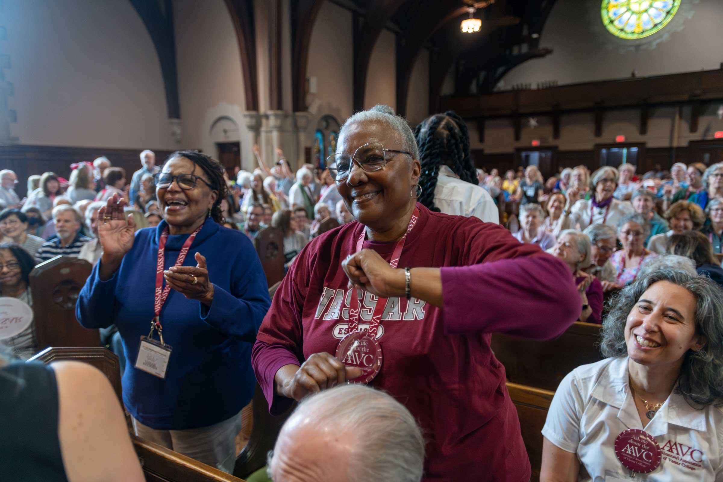 Two smiling people standing, dancing and clapping in a large mostly seated audience.