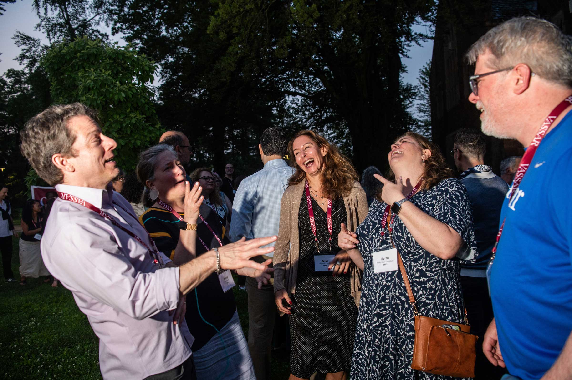 A group of people standing, laughing and talking outside at night.