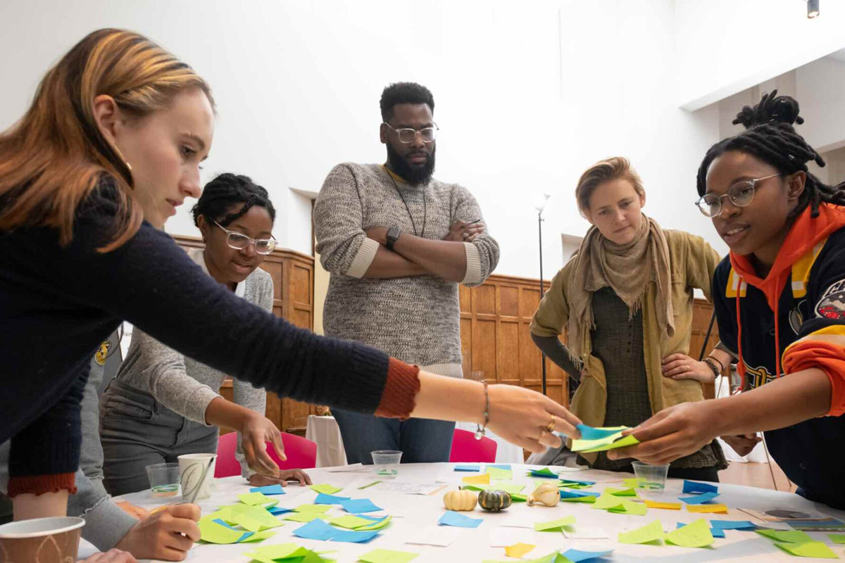 Group of people standing and sitting around a table sorting post-it notes.