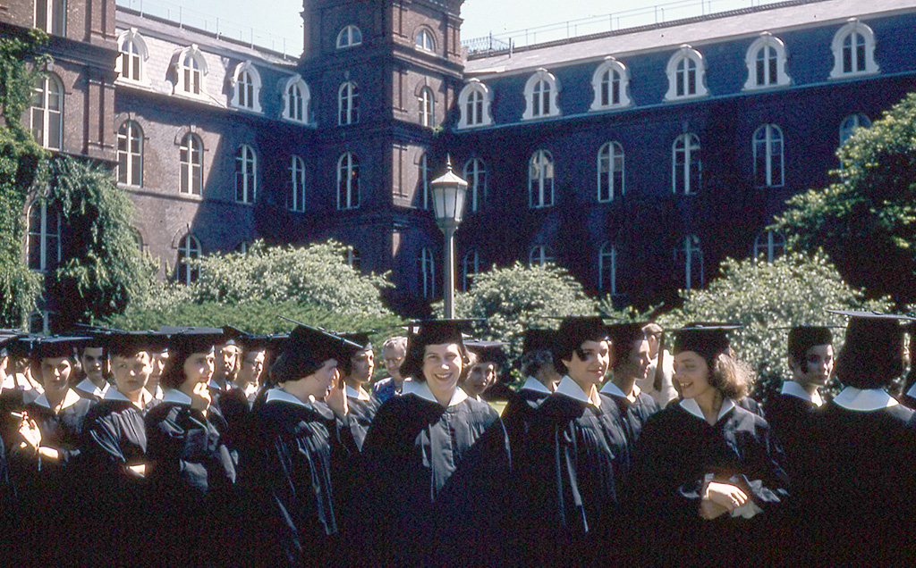 The graduating class in front of Main Building, with the subject in the center, smiling at the camera.