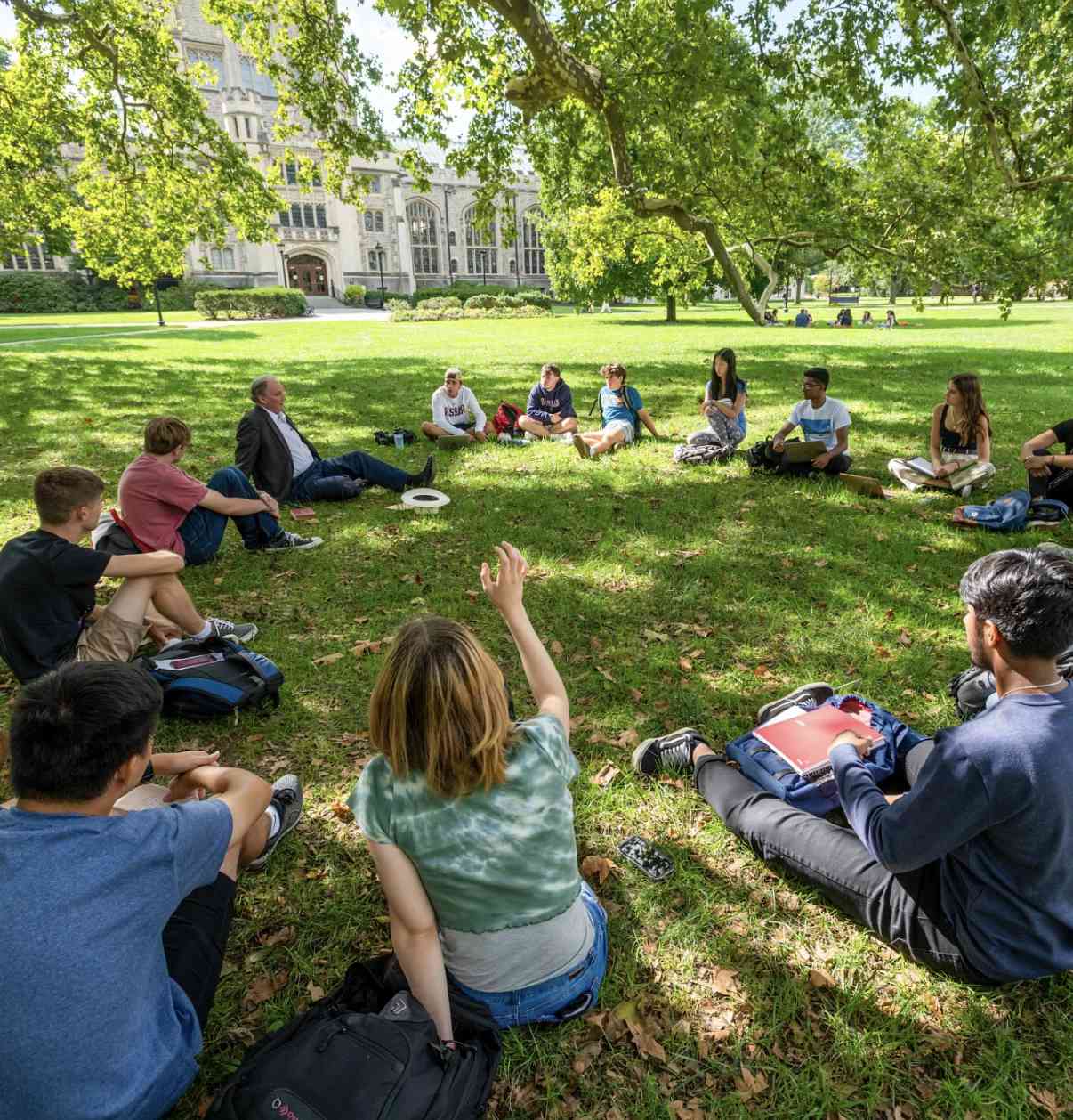 A group of students sit on a wide, grassy quad in front of the Vassar Library, a stone gothic building.