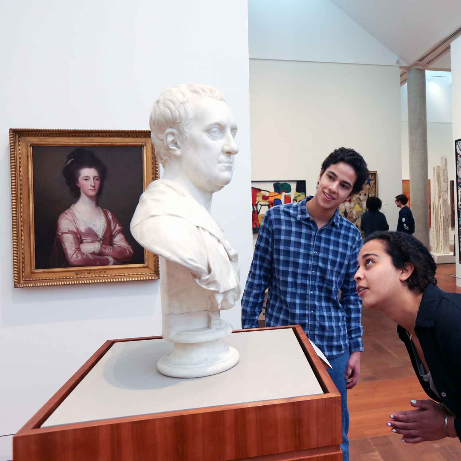 People in a gallery looking at bust or sculpture of a person's head.