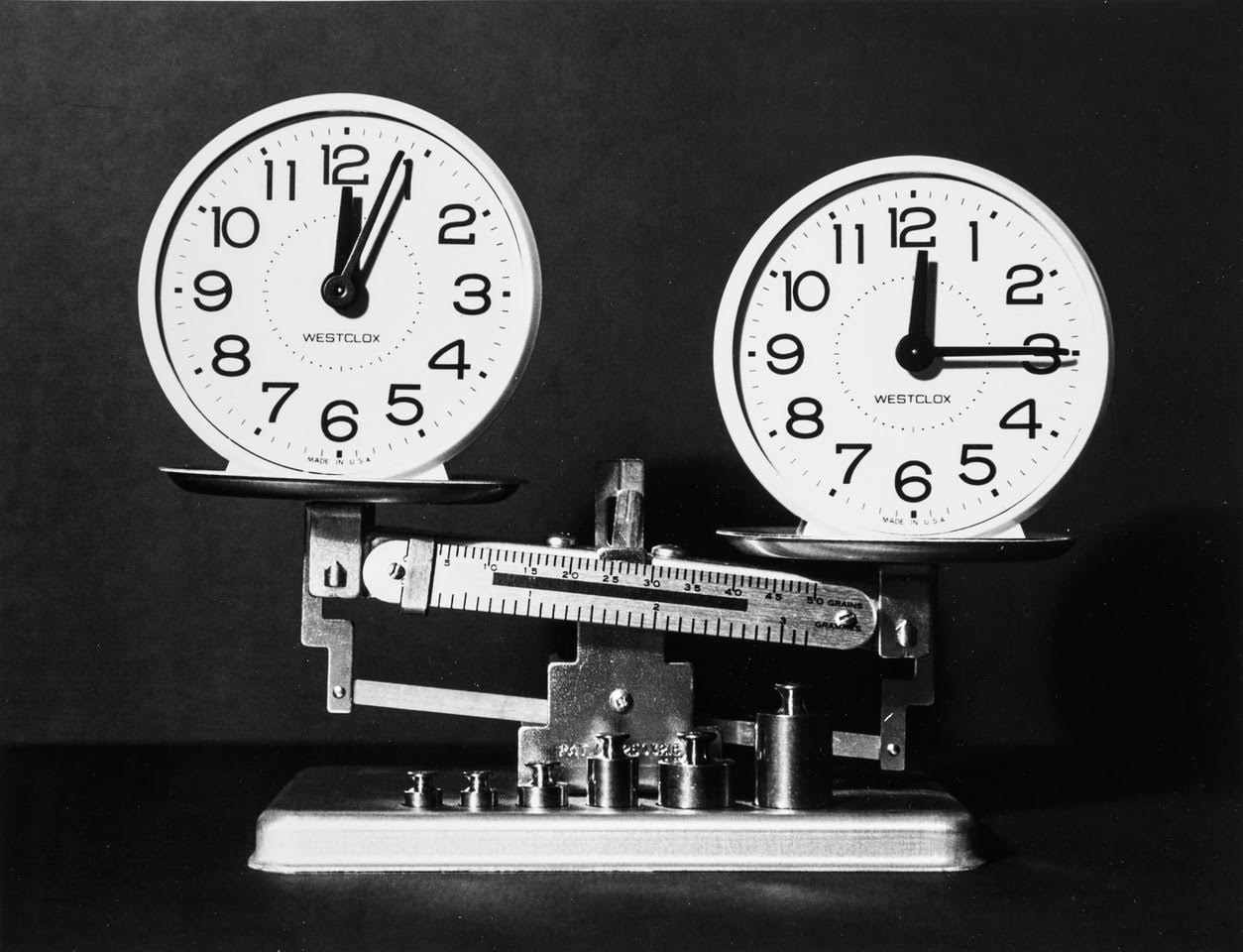 A black and white photograph of two clocks balanced on a scale.