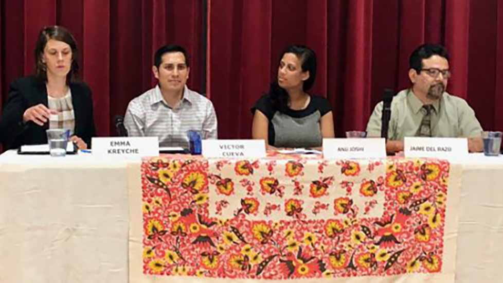 Four people sitting at the same side of a table with a curtain in the background.