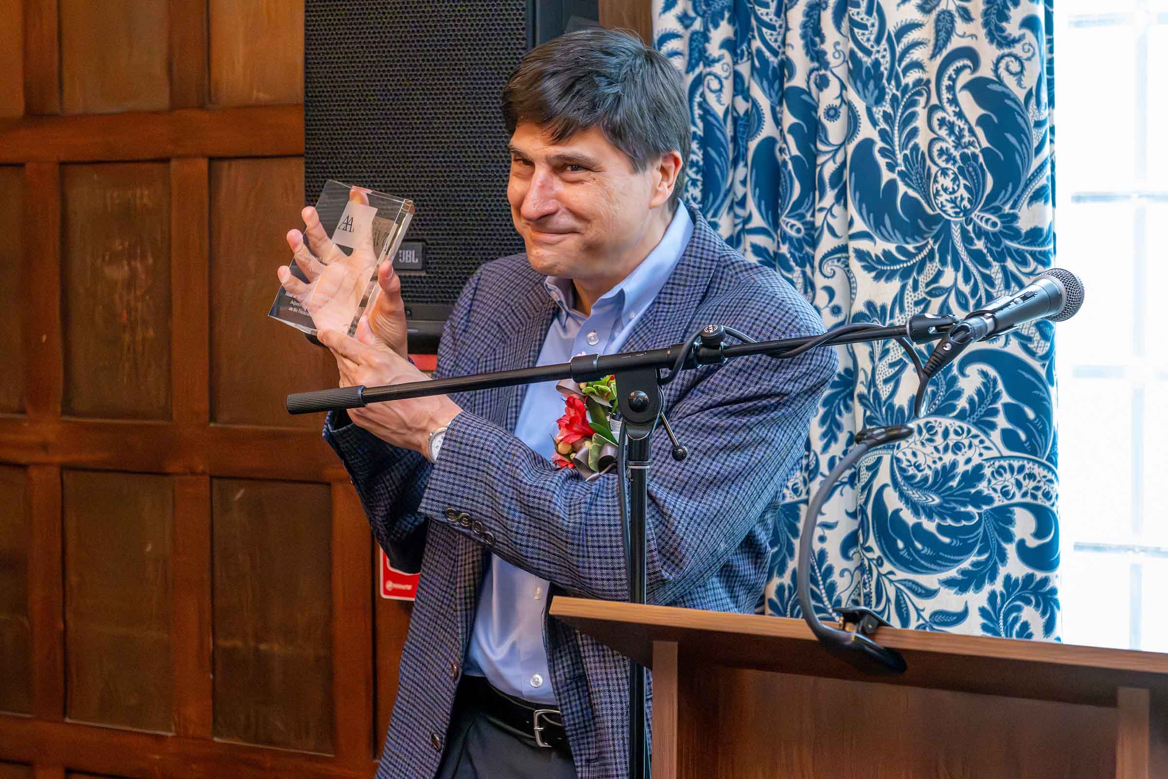Person standing and holding an award behind a lectern and microphone.