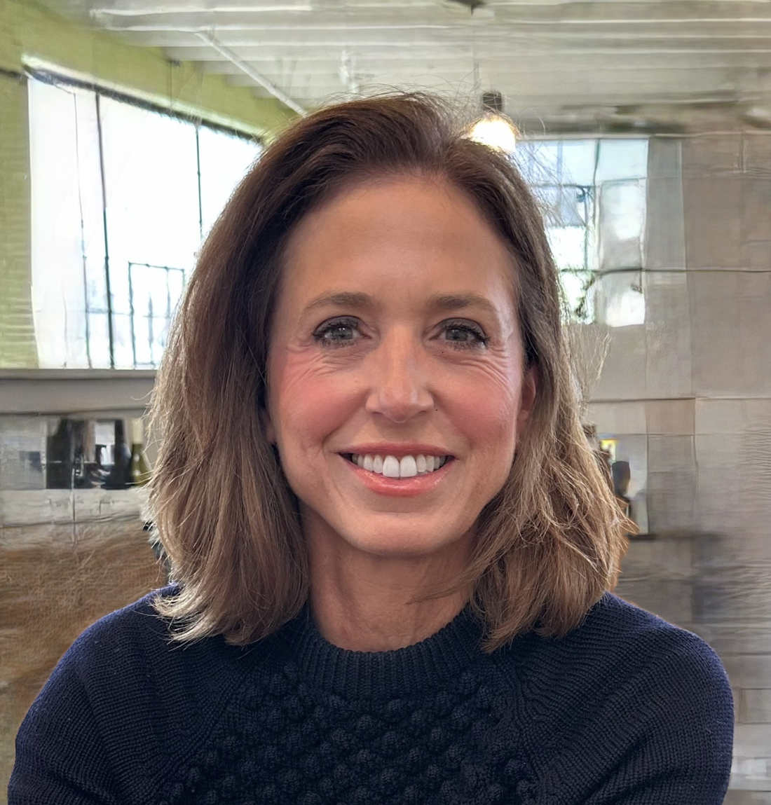 A portrait of Wendy Holcombe, a person with long brown hair and a navy blue sweater.