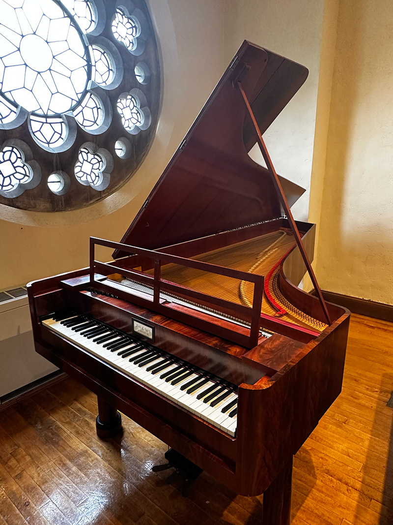 the Schubert era piano with the lid open, in front of a stained glass circular window.
