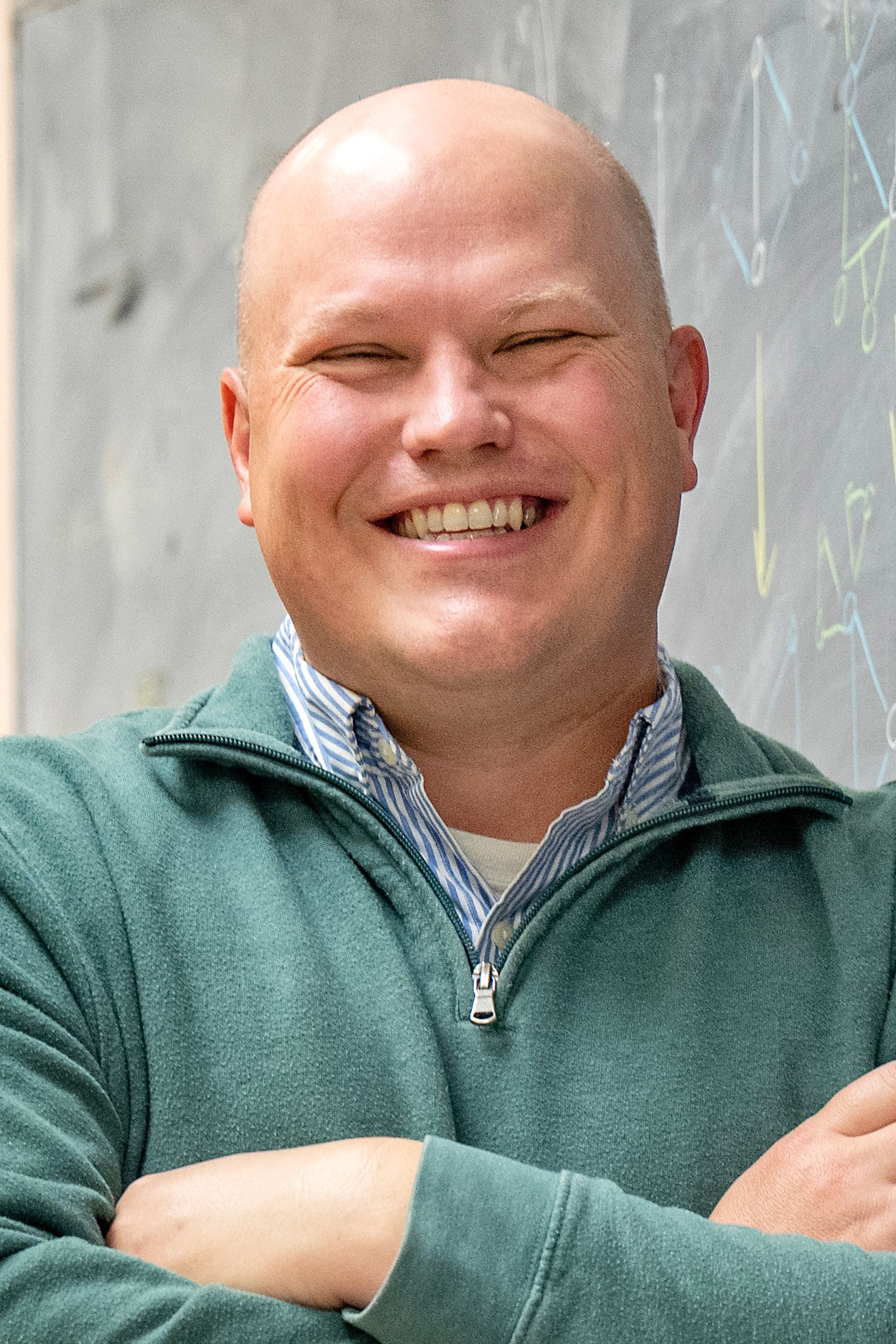 Portrait of a person standing in front of a green chalkboard with math equations written on it.