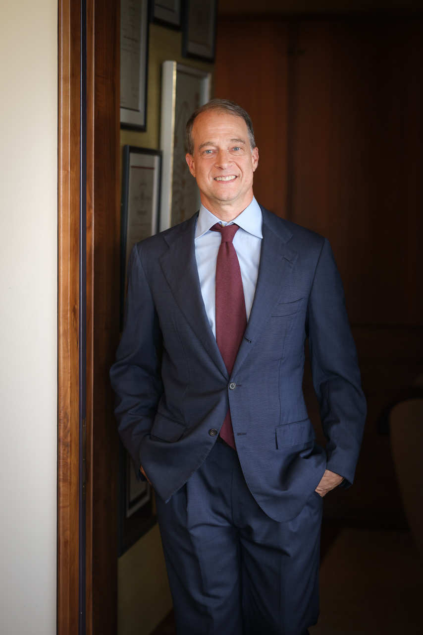 A portrait of Jon Friedland, a person in a dark blue suit with a red tie standing in a doorway.