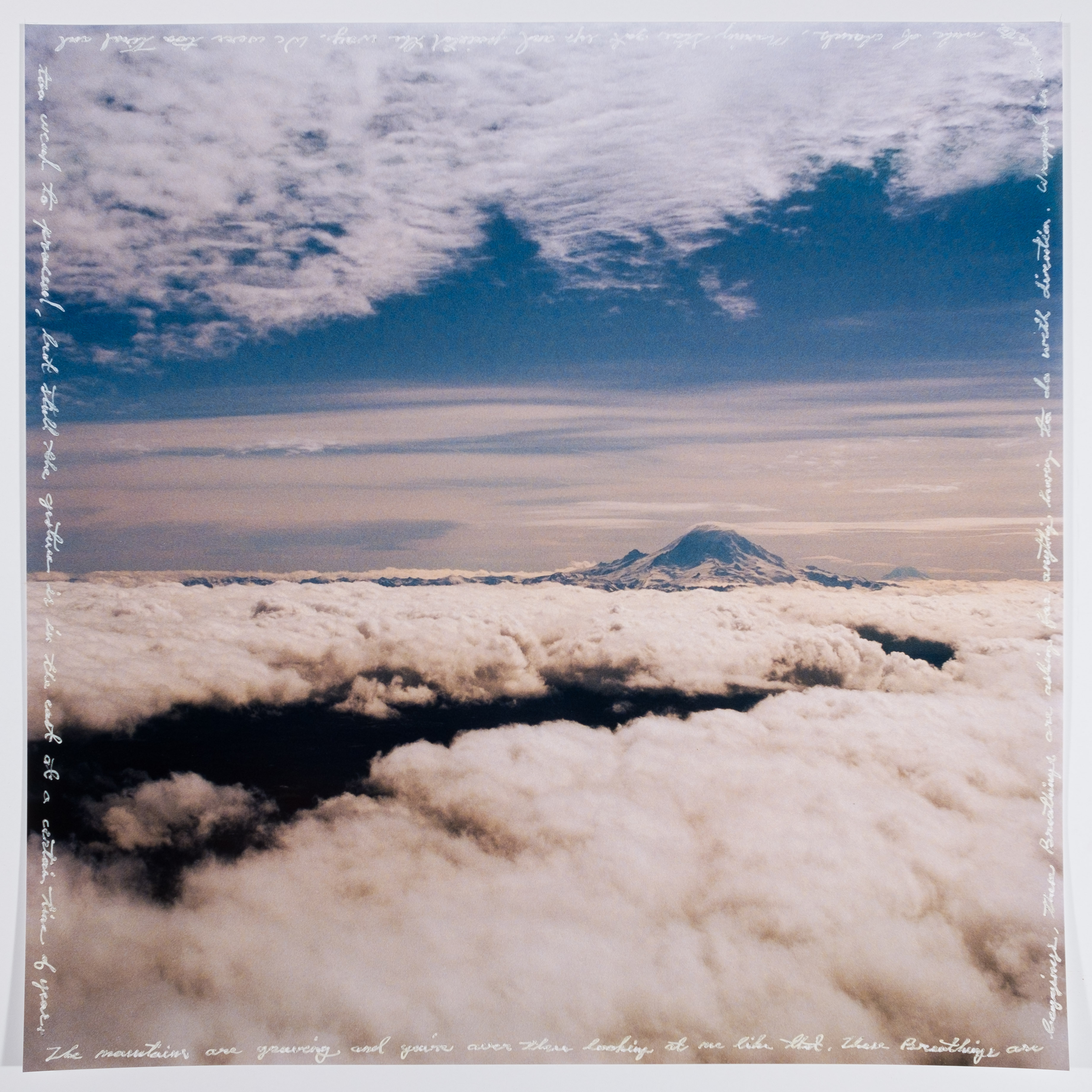 Photo of mountain poking through clouds, framed by white cursive text