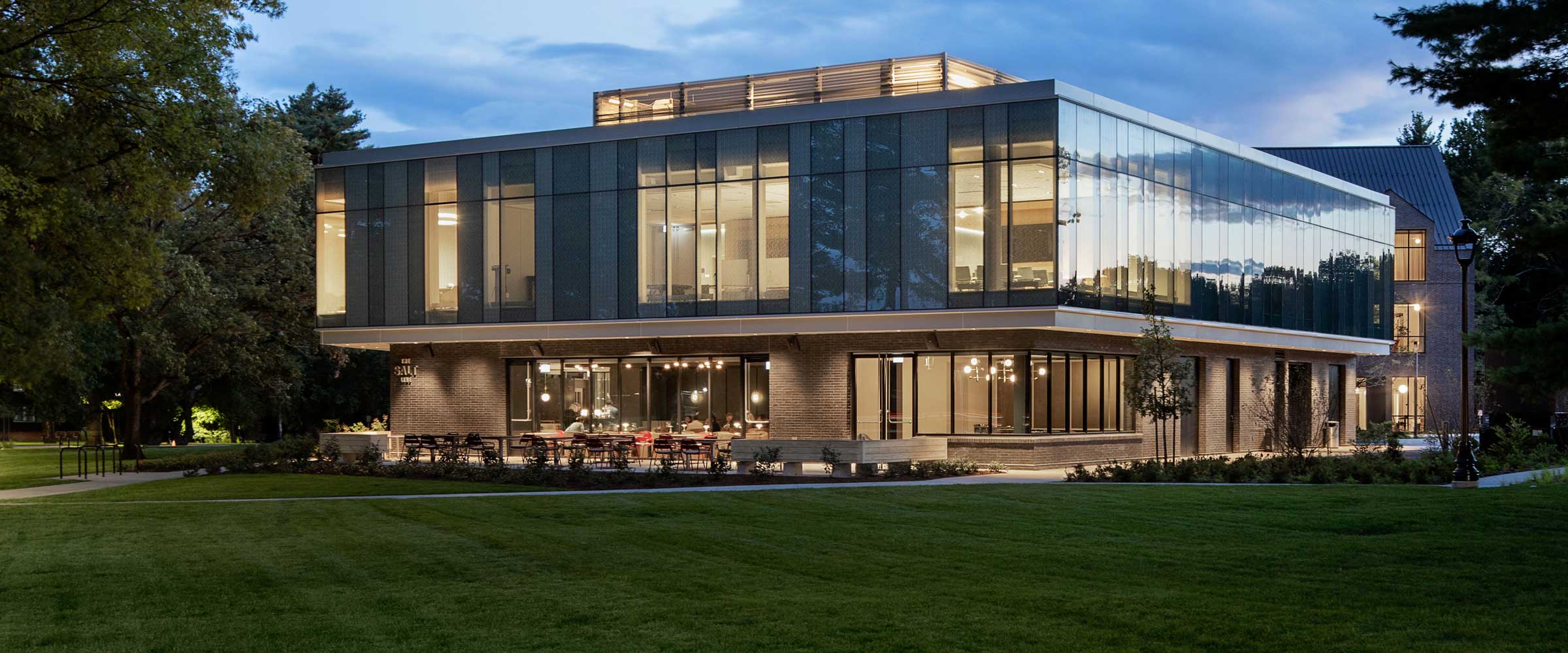 Glass and concrete buildings nestled within trees with foliage reflecting on the windows.