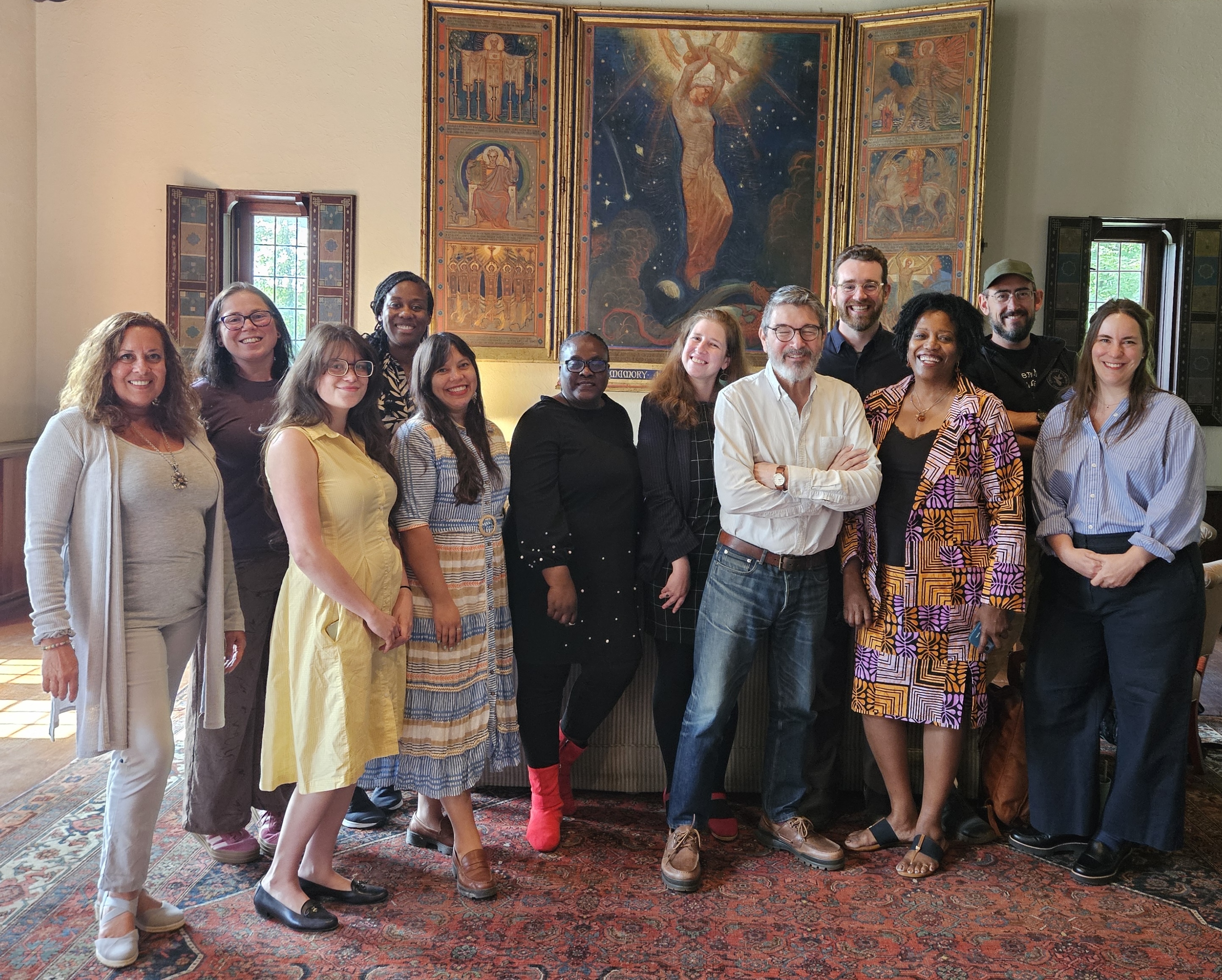 A group of people smiling at the camera and standing in an ornate room with paintings and Persian rugs.