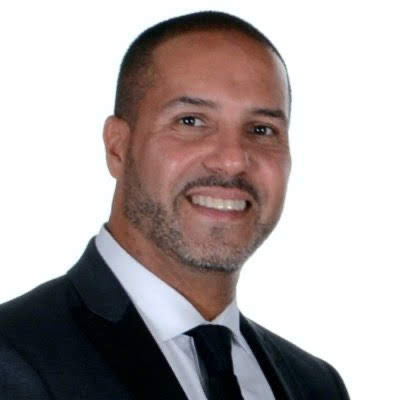 Salvador Contes in a dark suit, white dress shirt, and black tie, posed against a plain white background.