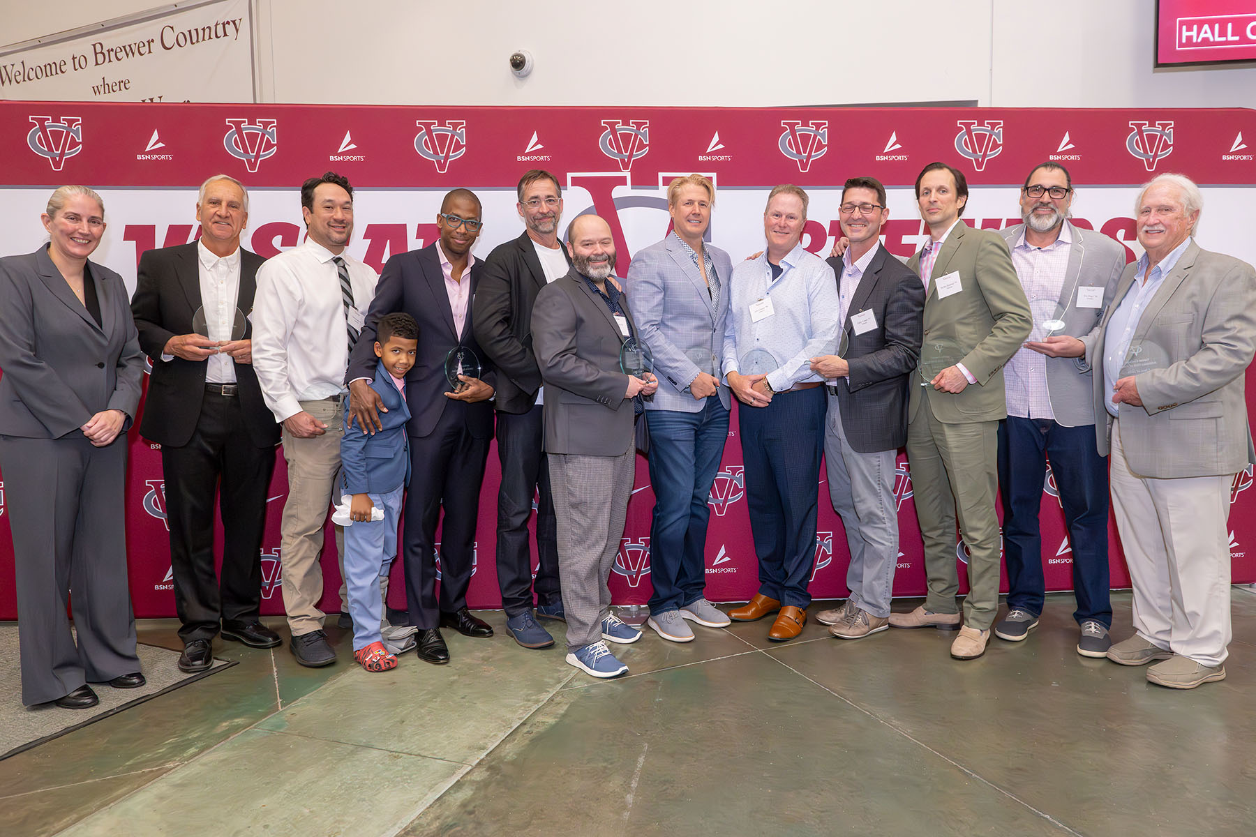 Group of honorees posing with awards standing in front of a maroon Vassar backdrop.