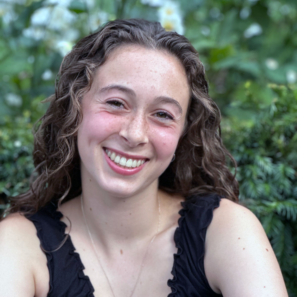 Photo portrait of someone in front of a green shrub.