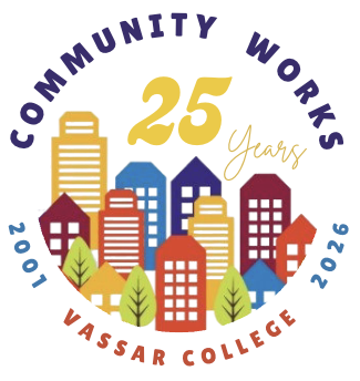 A circular logo featuring a colorful cityscape with stylized buildings in shades of red, orange, yellow, and blue, arranged behind a row of five green trees. Above the buildings, bold yellow text reads “25” with the word “Years” in a script font to the right. Arched purple text at the top reads “COMMUNITY WORKS,” while the years “2001” and “2026” curve along the sides. At the bottom, “VASSAR COLLEGE” is written in uppercase red letters.