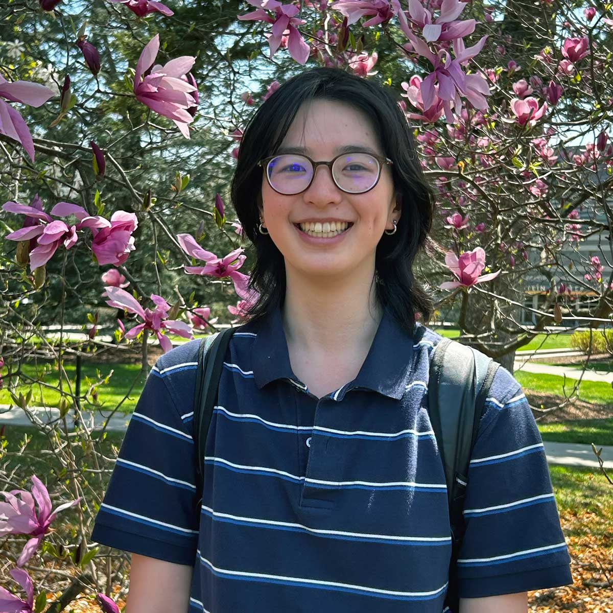 Photo portrait of a person standing in front of cherry blossom trees.