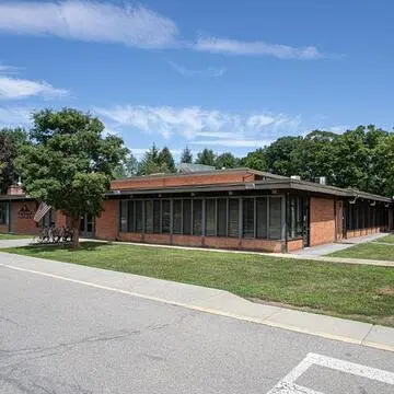 Exterior of a building surrounded by trees, grass, and a parking lot.