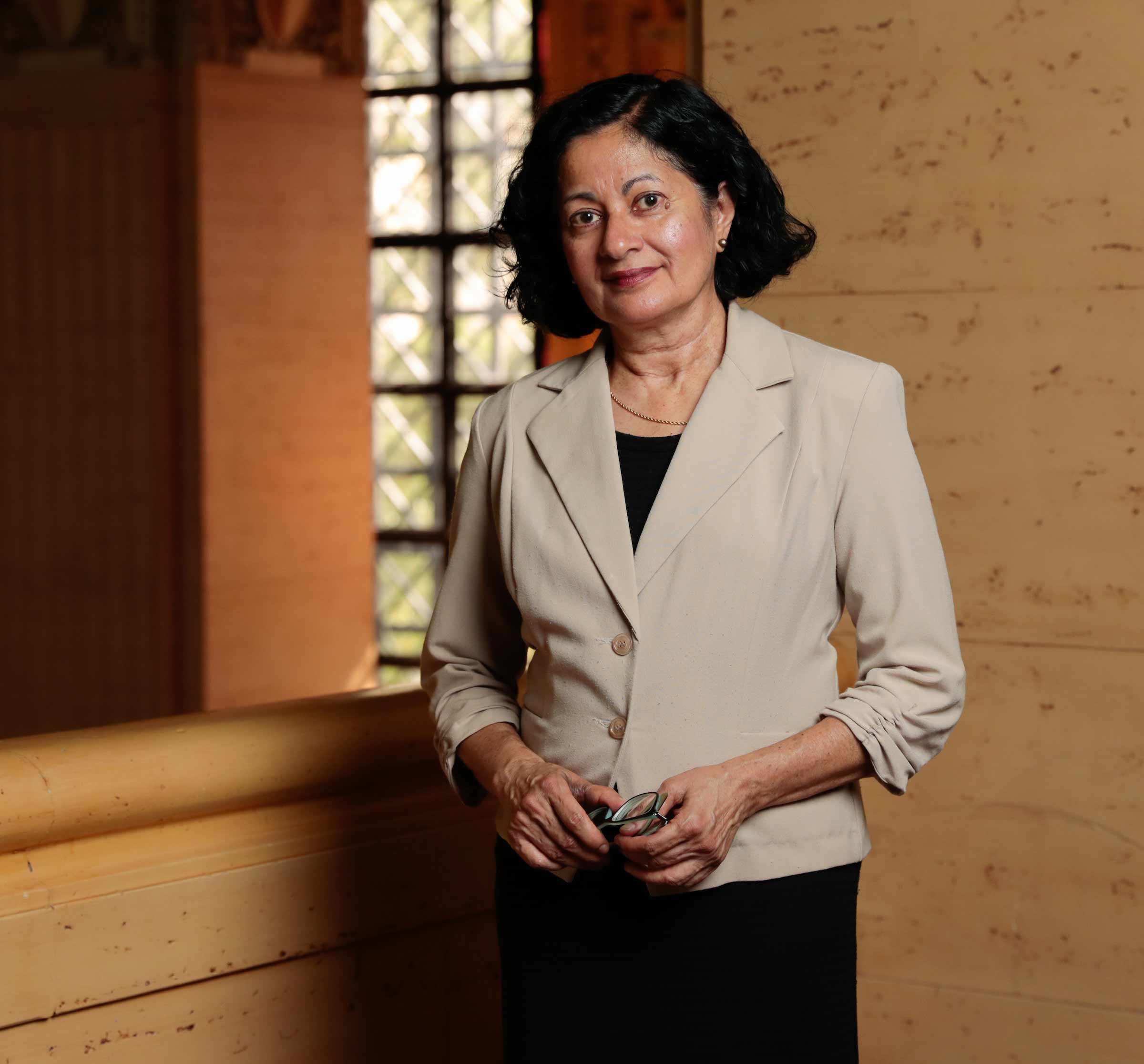 A portrait photo of Jyotsna Vaid posing in front of backlit ornate windows.