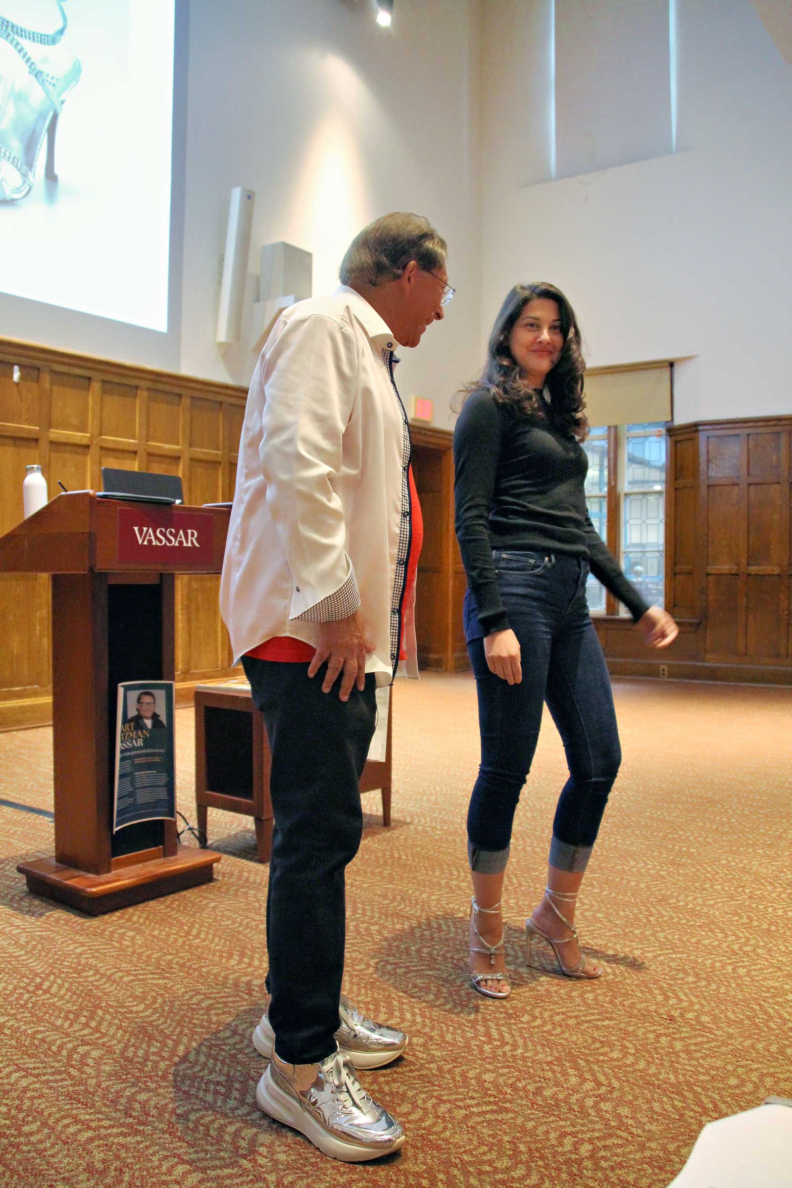 Two people standing before an audience with a projection screen behind them.