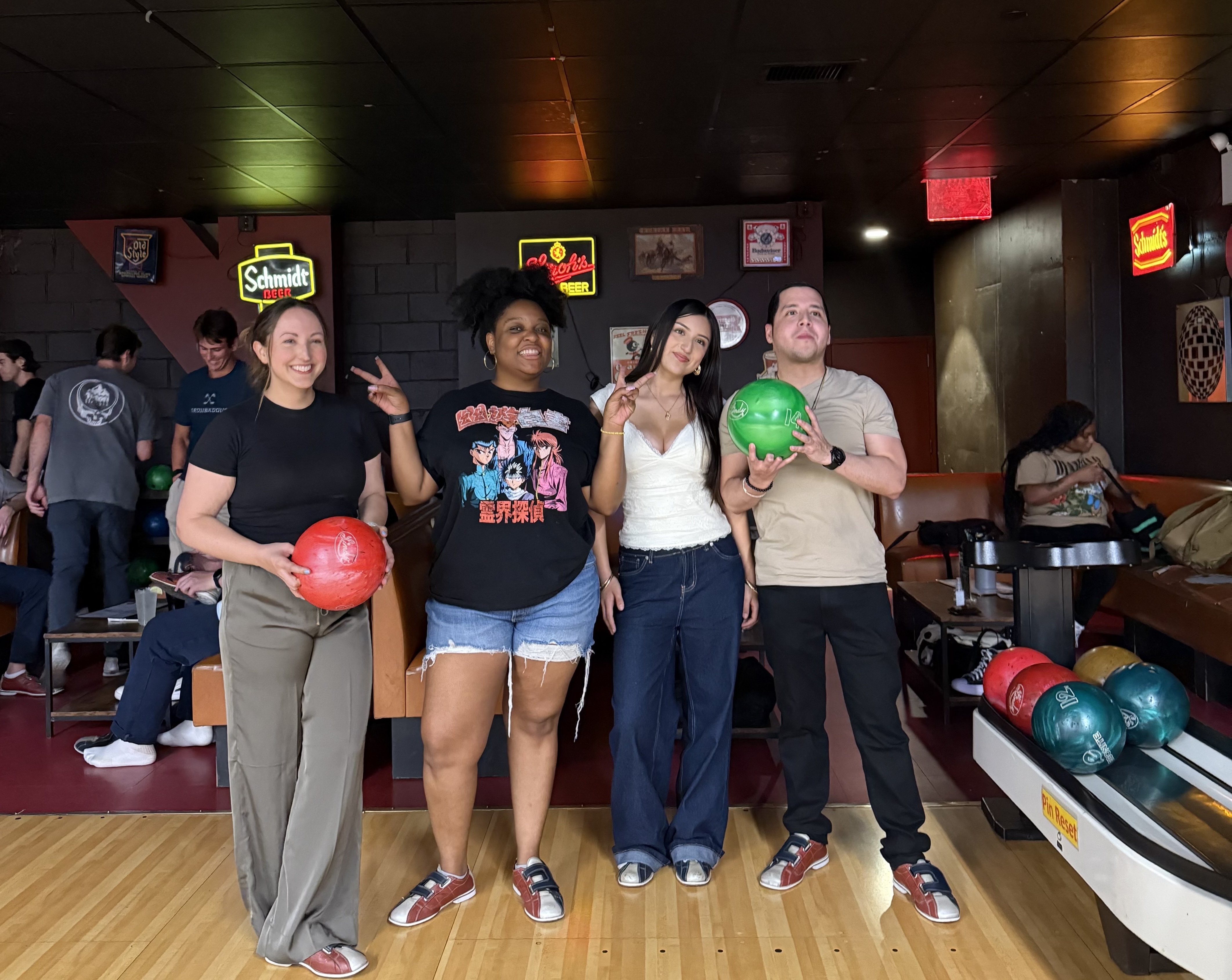 Four people smile in a bowling alley, with two holding bowling balls.