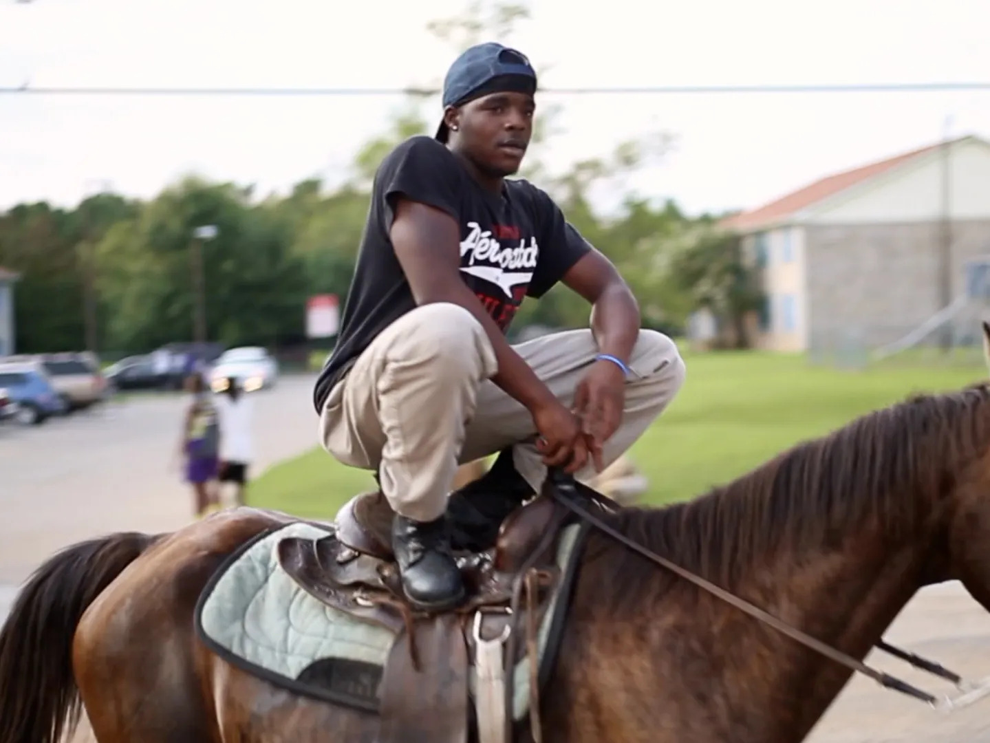 A a still from the film Hale County This Morning, This Evening featuring one of the subjects, a person crouching while standing on the saddle of a horse.