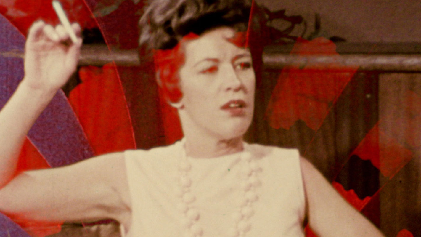 Film still of a close up of a seated person holding a cigarette while looking on.
