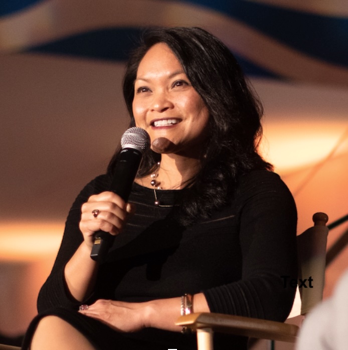 Smiling person seated and holding a microphone.