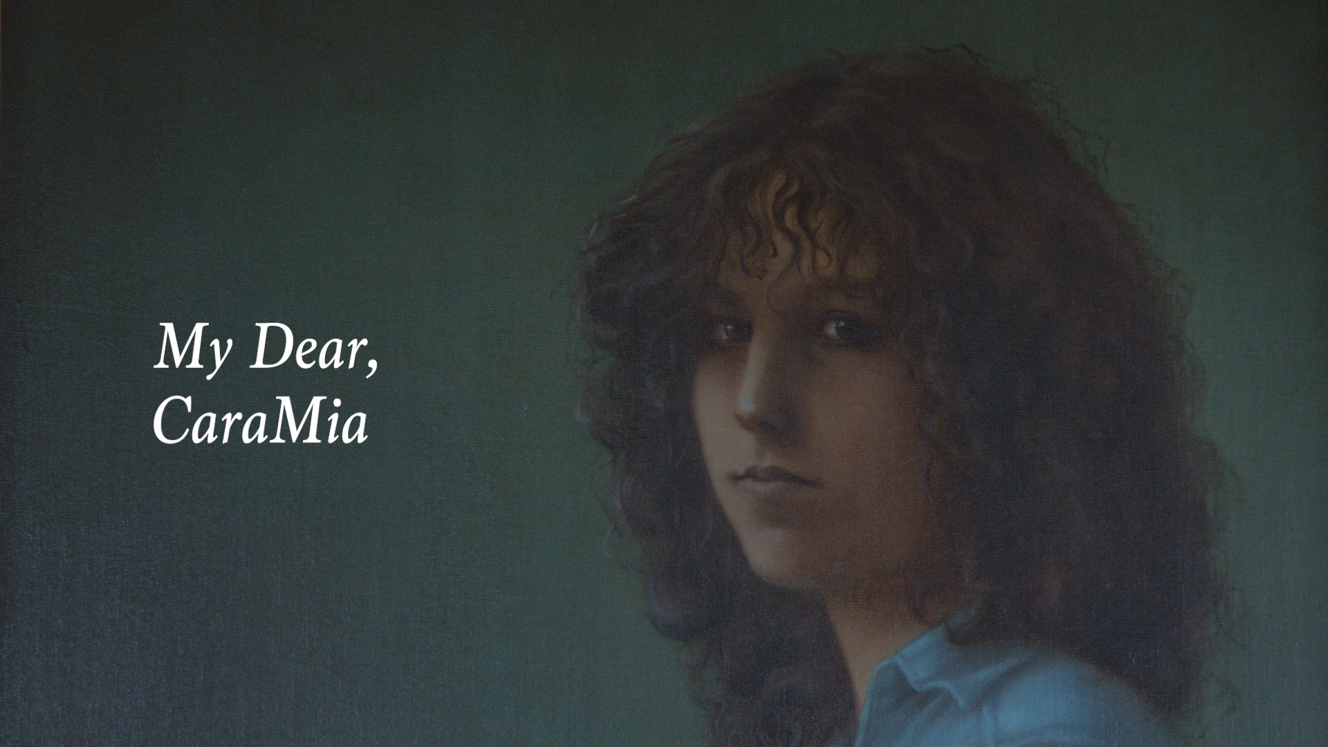 A realistic painted portrait of a person with long, voluminous dark brown curls, facing forward with a calm, neutral expression. Their face is softly illuminated, revealing subtle shadows across the cheeks and neck. They wear a light blue shirt with a visible collar, and the background is a textured, dark green gradient. On the left side of the composition, serif white text reads “My Dear, CaraMia.”