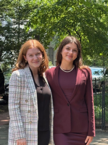 A photo of Anne Wallar ’26 and Charlotte Tanner-Morash ’26, standing together and smiling. Both have long hair; Wallar, right, has red hair and wears a white checked shirt. Tanner-Morash, left, wears a burgundy shirt and has long brown hair.