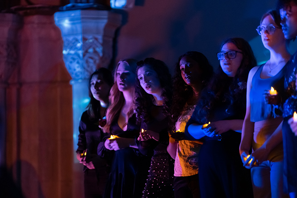 Detail of performers on a dramatically lit stage, holding candles.