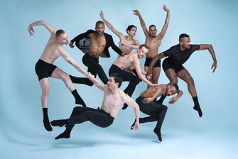 A dynamic cluster of figures is captured mid-motion against a soft blue background. Individuals are dressed in varying styles of form-fitting attire, including shorts and fitted tops, some are topless, showcasing diverse postures and angles as they leap and twist through the air. The composition demonstrates a sense of movement and fluidity, with arms extended and legs bent in various directions, creating an energetic scene. Subtle lighting enhances the contours of each figure.