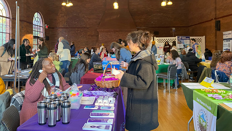 Candid photo of a community fair, with tables for different organizations with attendees in conversation with people at their tables.