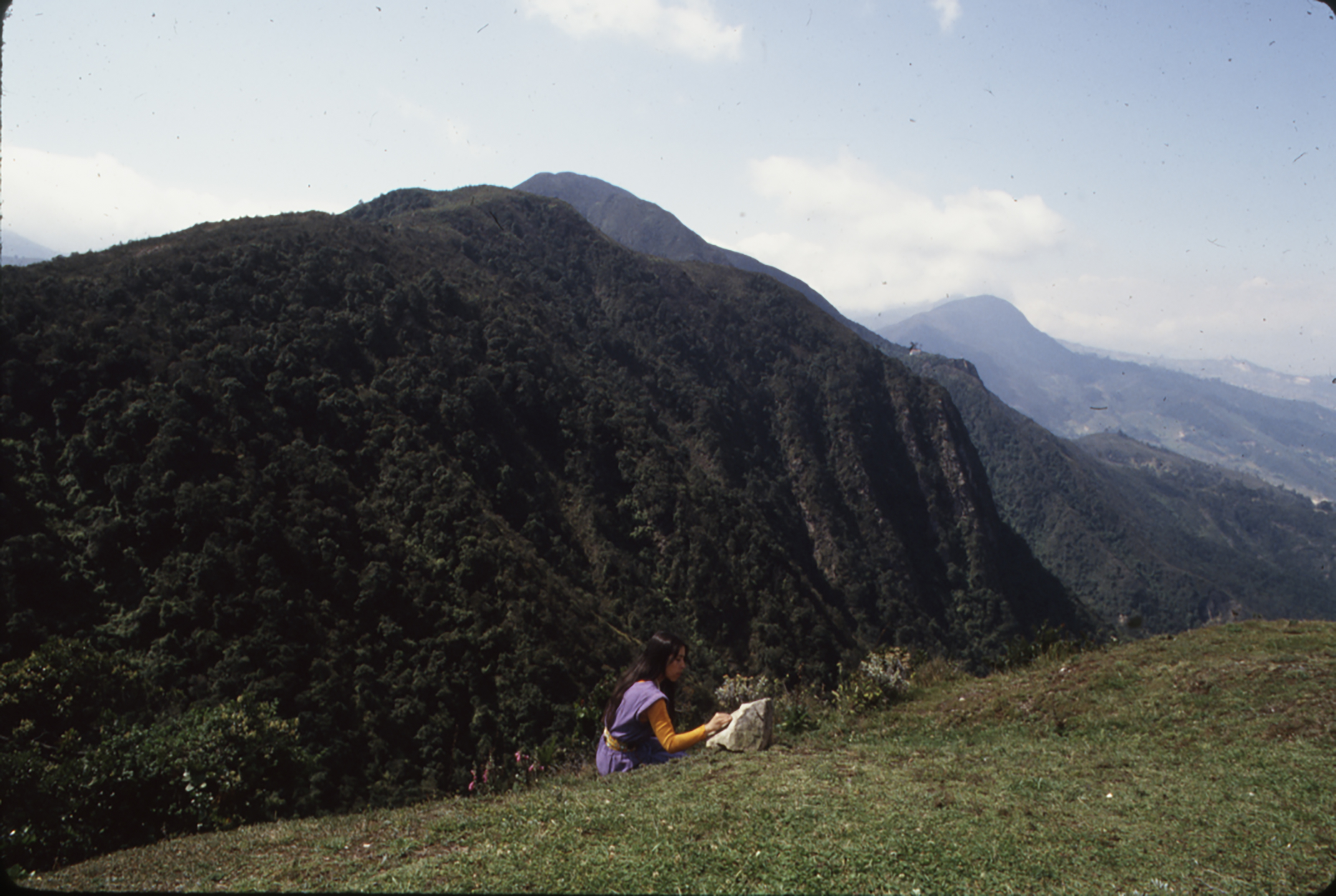 Photo of woman seated writing poetry with tall mountains in the background