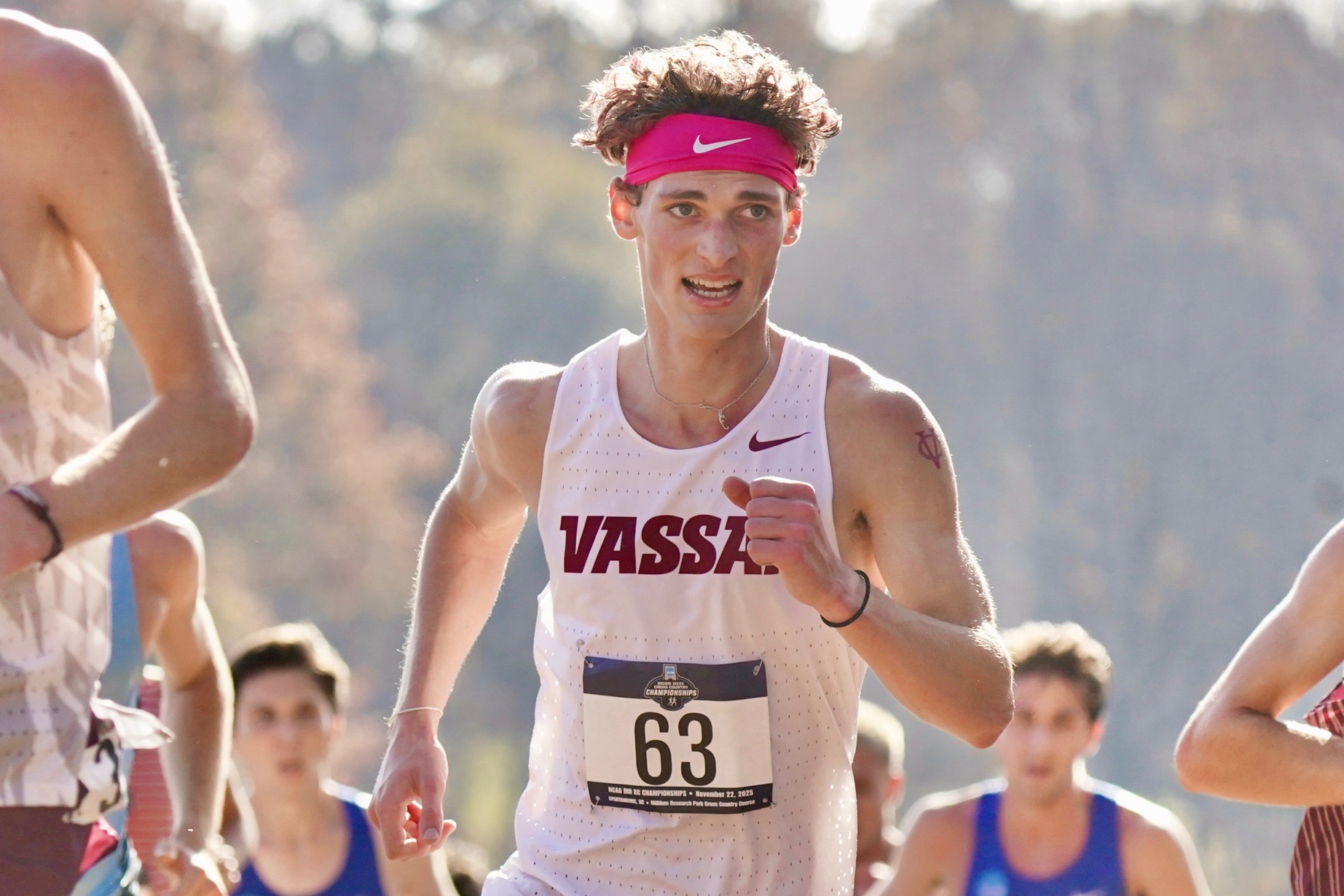 closeup of a runner in the middle of a race, wearing a headband across his forehead and Vassar tank top.